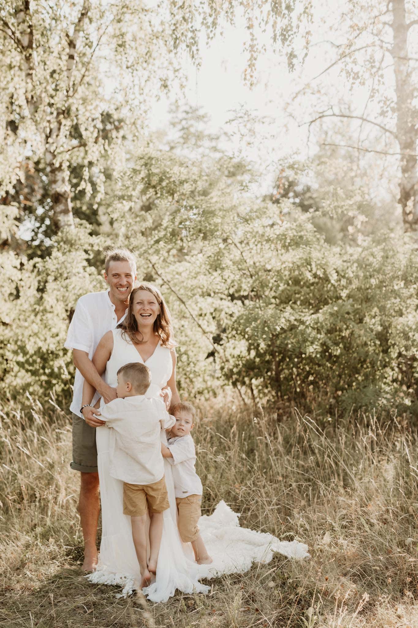 Familie knuddelt und lacht beim Babybauch Fotoshooting in einer Wiese