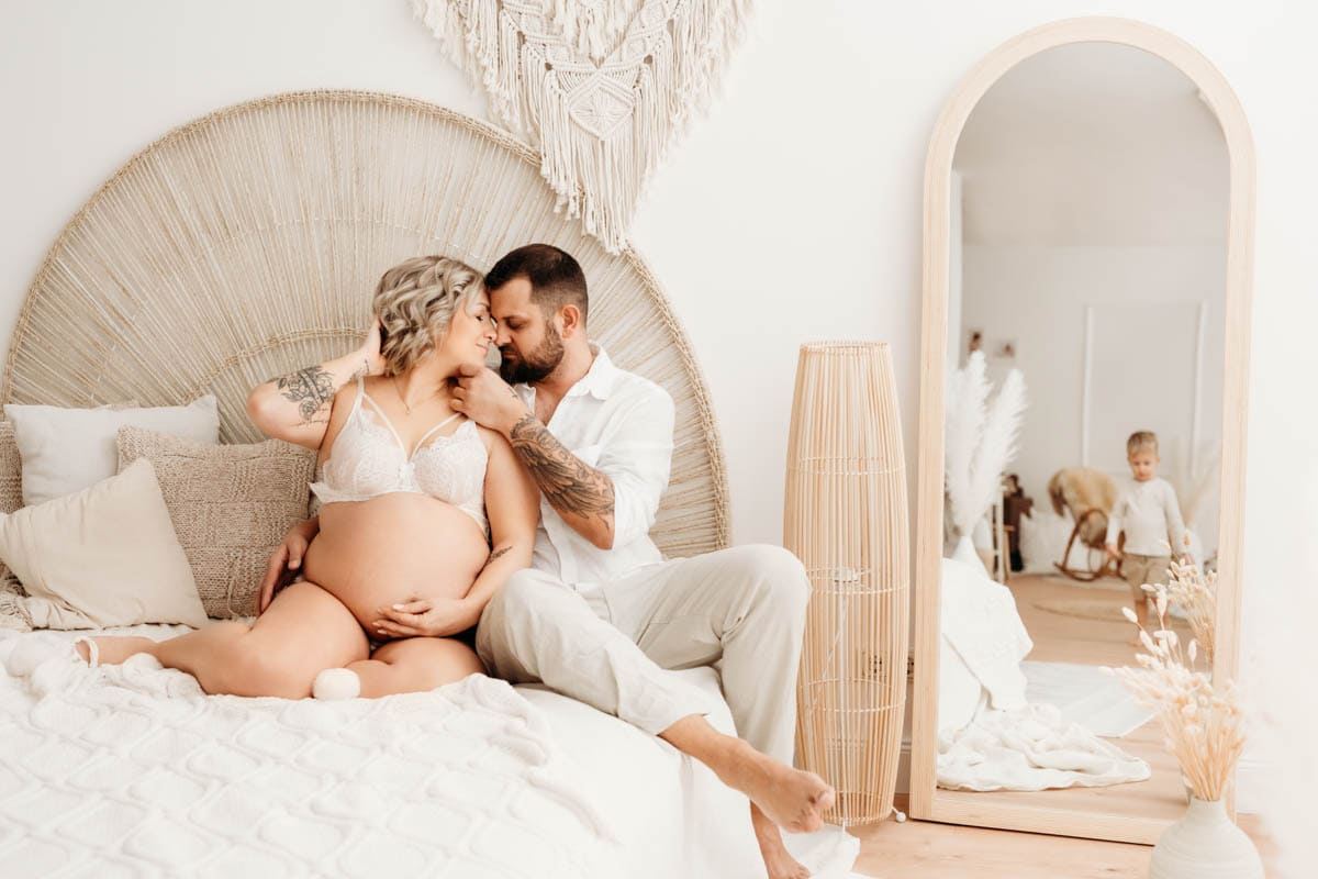 Schwangere Frau mit Mann küssen sich am Bett im Boho Studio