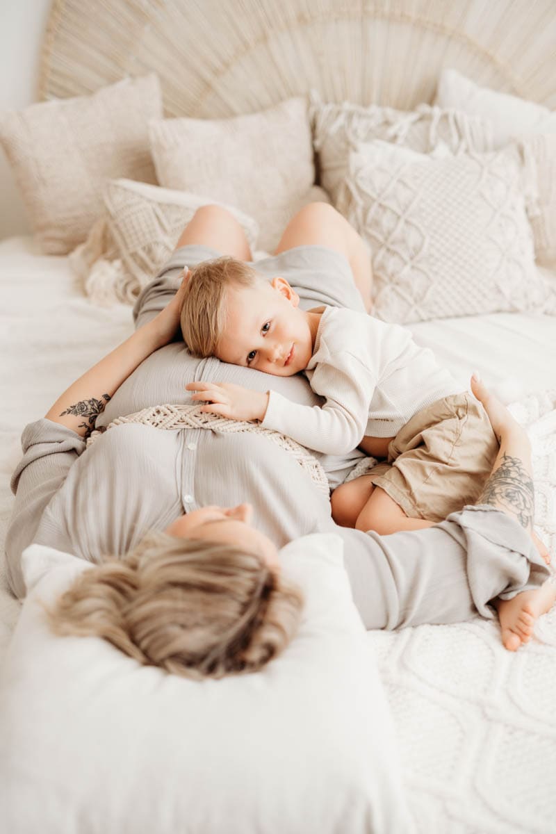 Beim Babybauchshooting kuschelt Mama mit Geschwisterkind am Bett