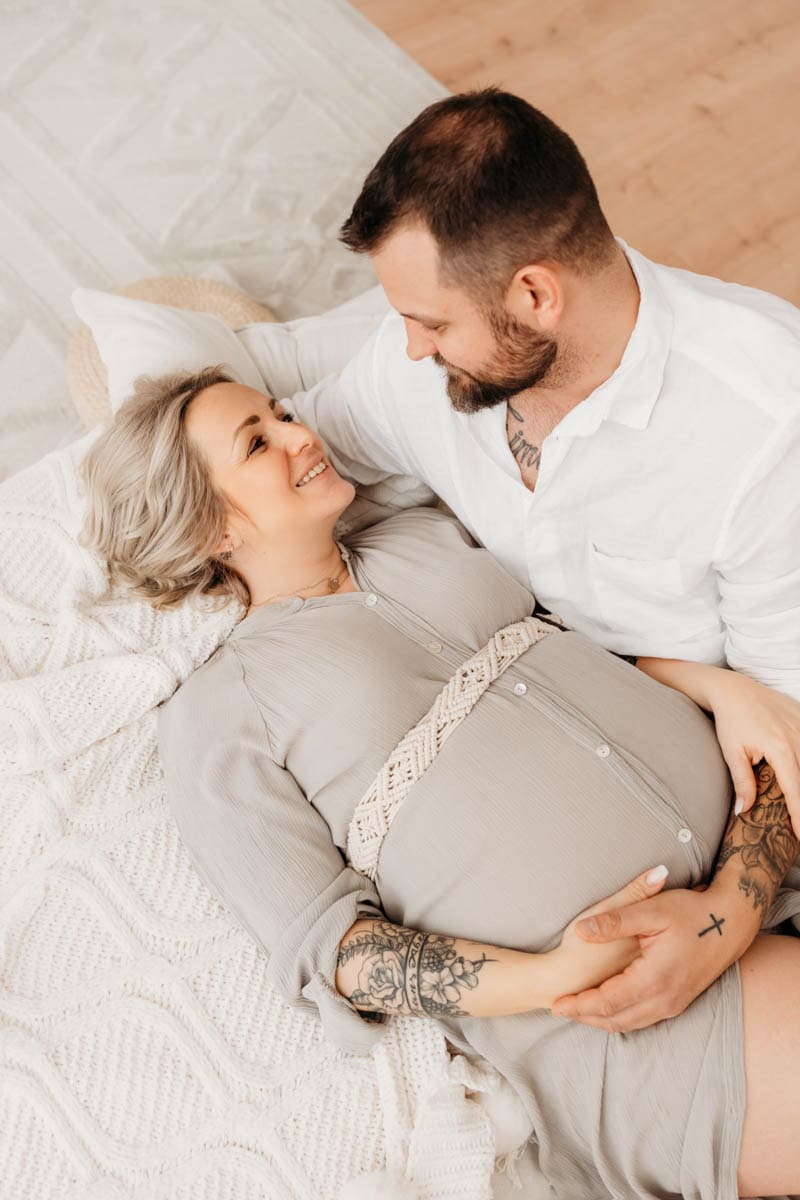 Mann sieht seiner schwangeren Frau beim Kuscheln am Bett ganz tief in die Augen.