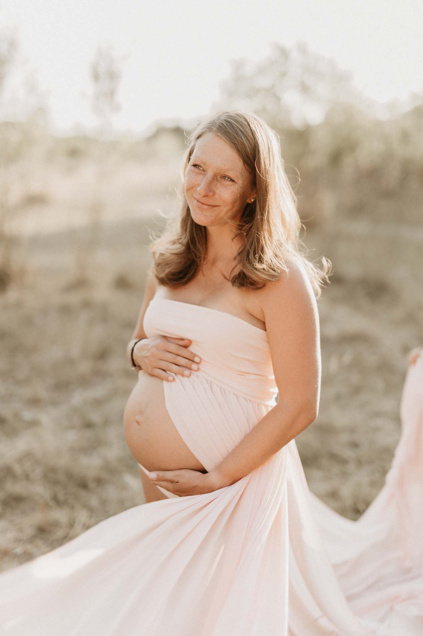 Schwangere Frau mit fliegendem rosa Kleid