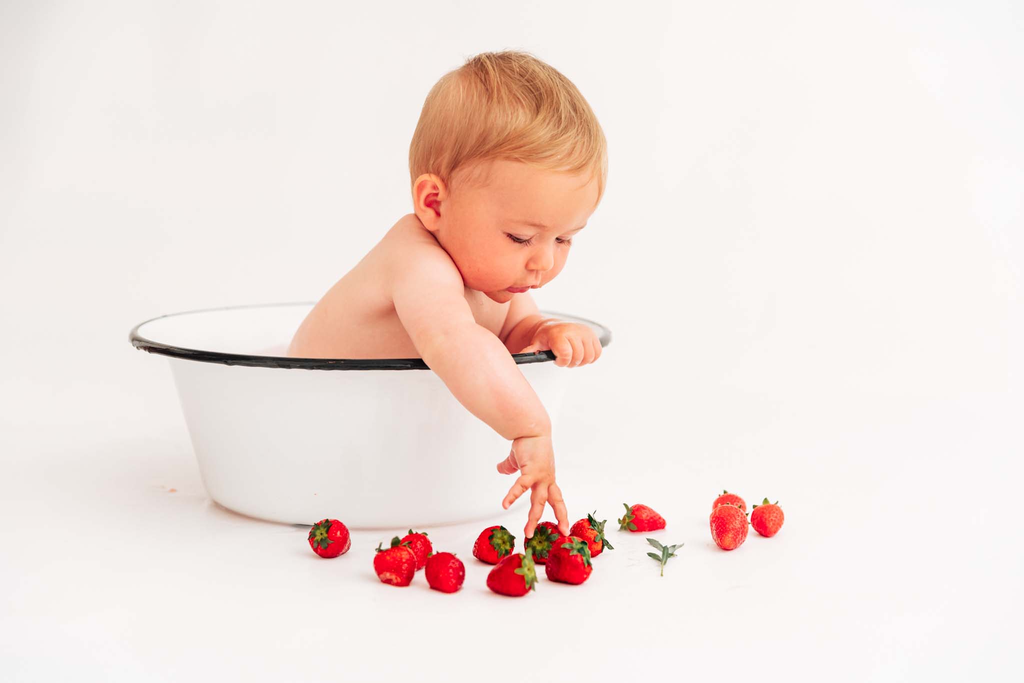 Kind leht sich über Wanne und stibitzt sich eine Erdbeere beim Babyshooting München Kind greift nach Erdbeere beim Babyshooting