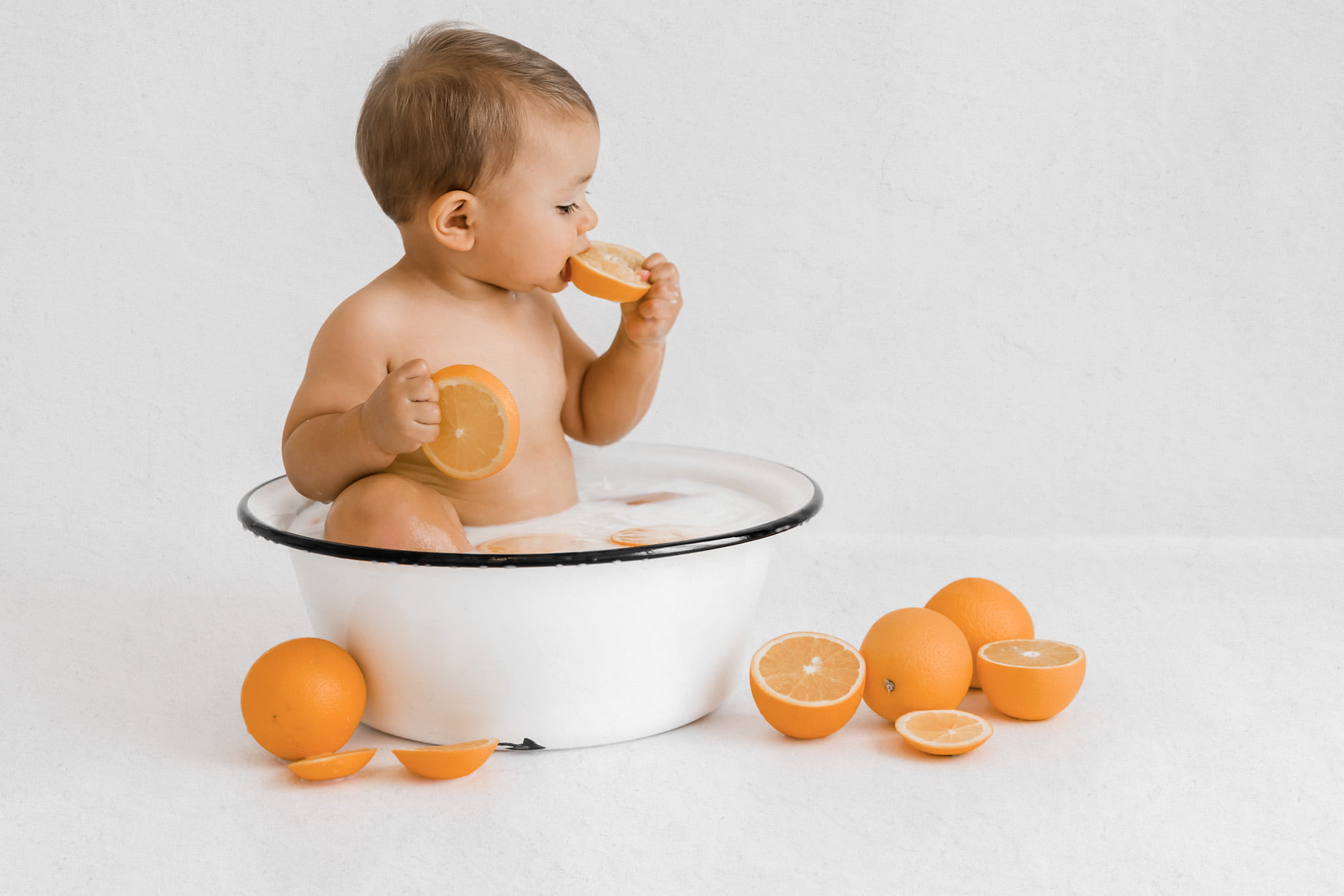 Milchbad-Shooting im Orangenbad Baby beißt in Orange beim Baby Fotoshooting