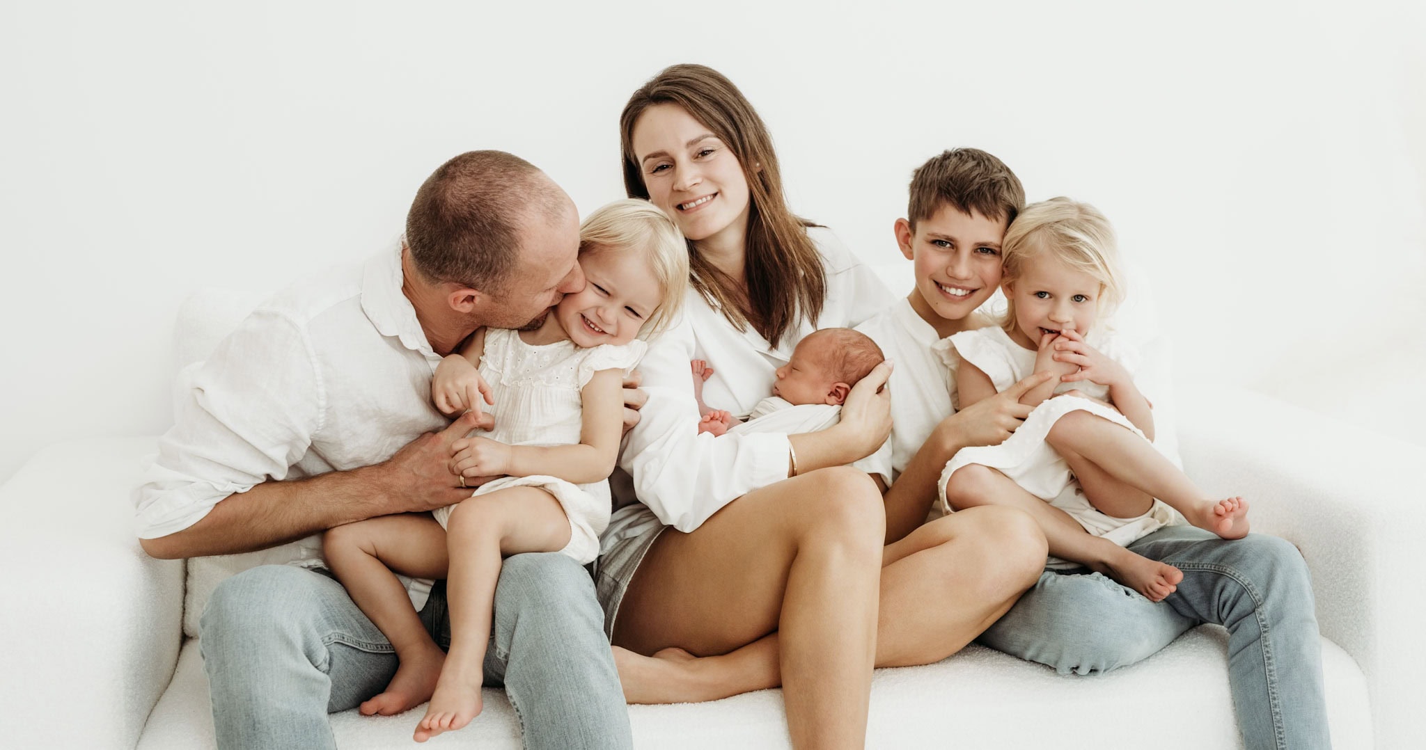 Großfamilie mit neugeborenem Baby beim Kuscheln und lachen auf der Couch