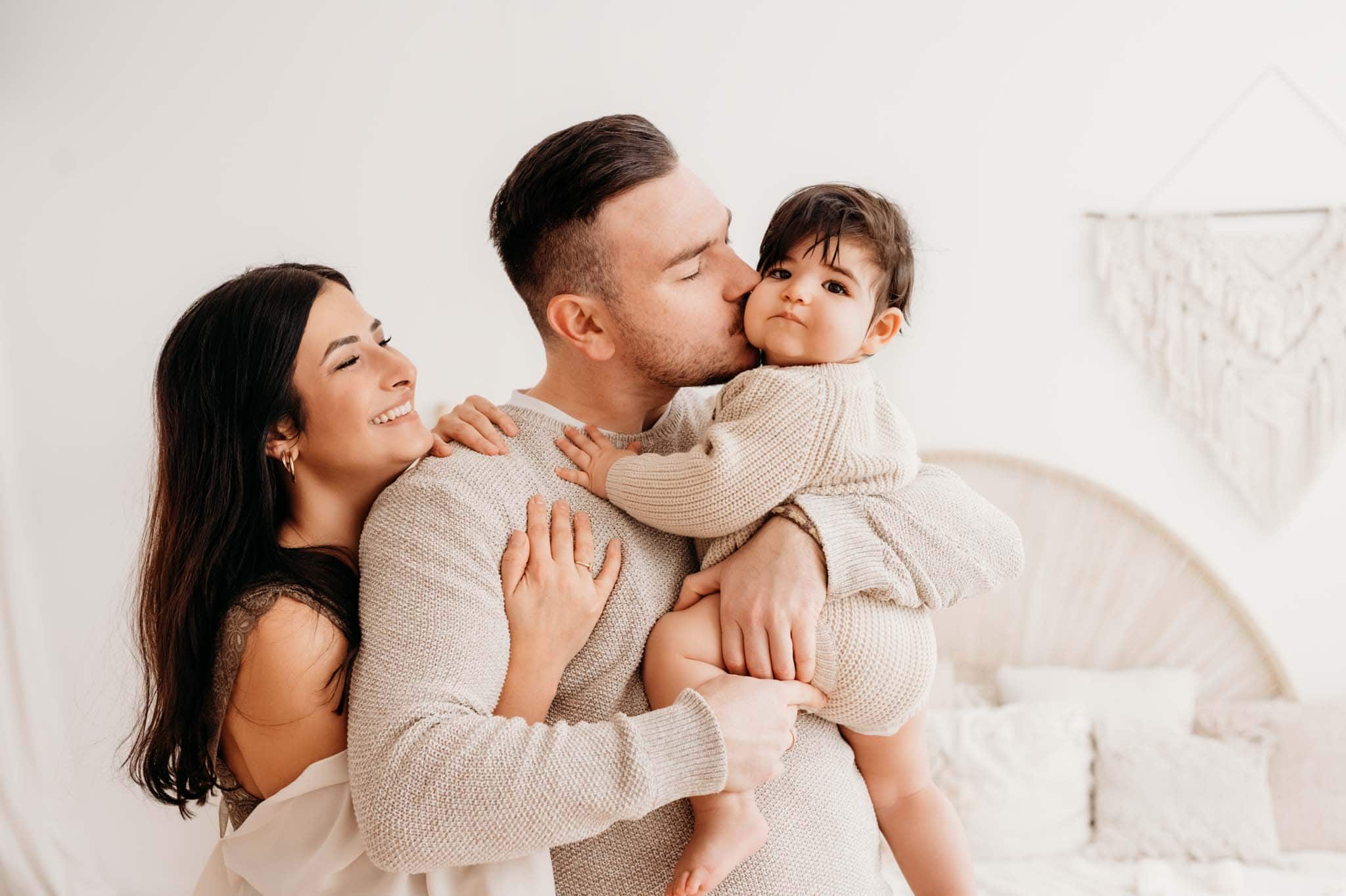 Papa küsst Baby auf die Backe beim Familienportrait