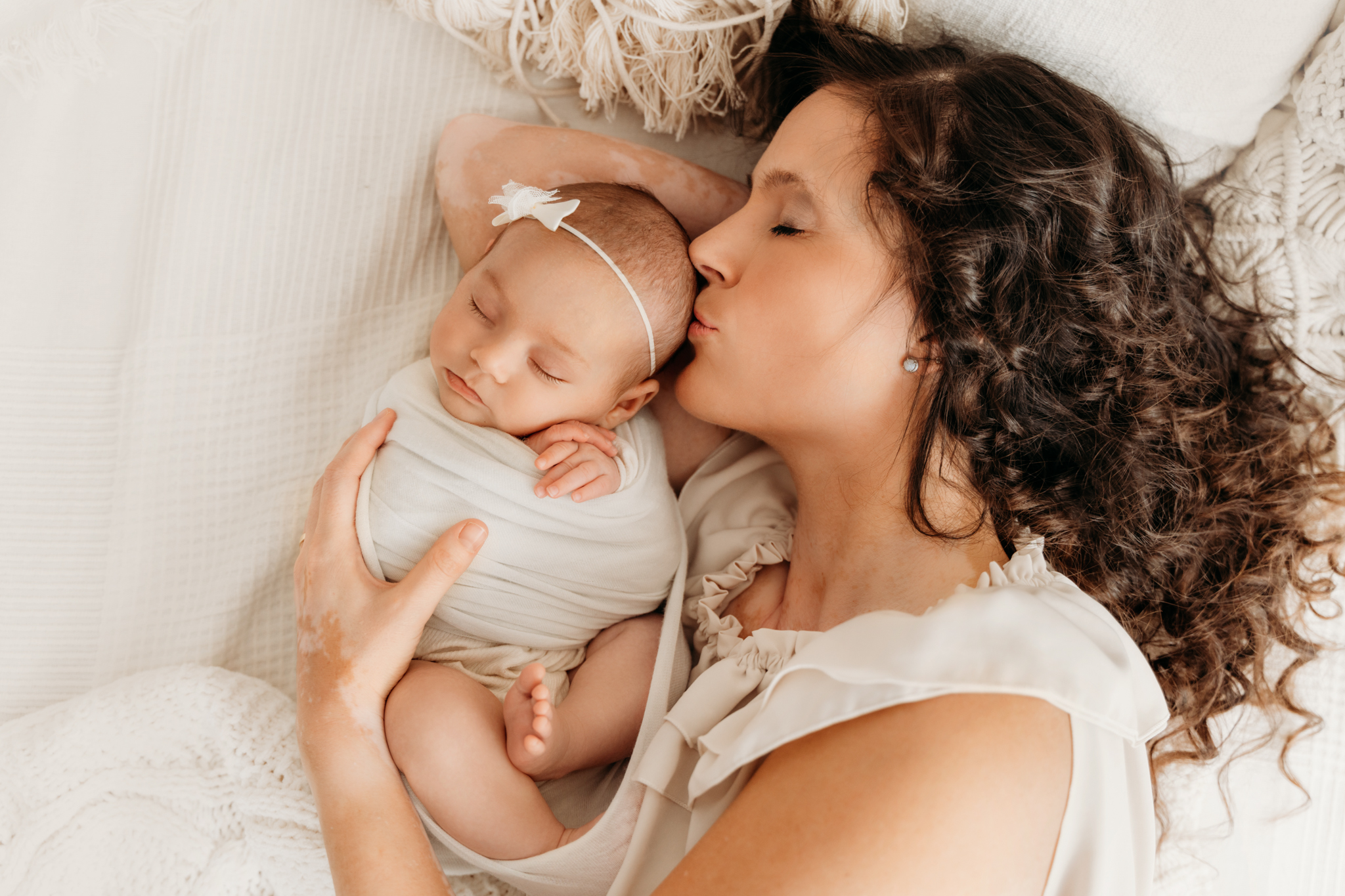 Mama küsst kuschelnd neugeborenes Baby auf Stirn