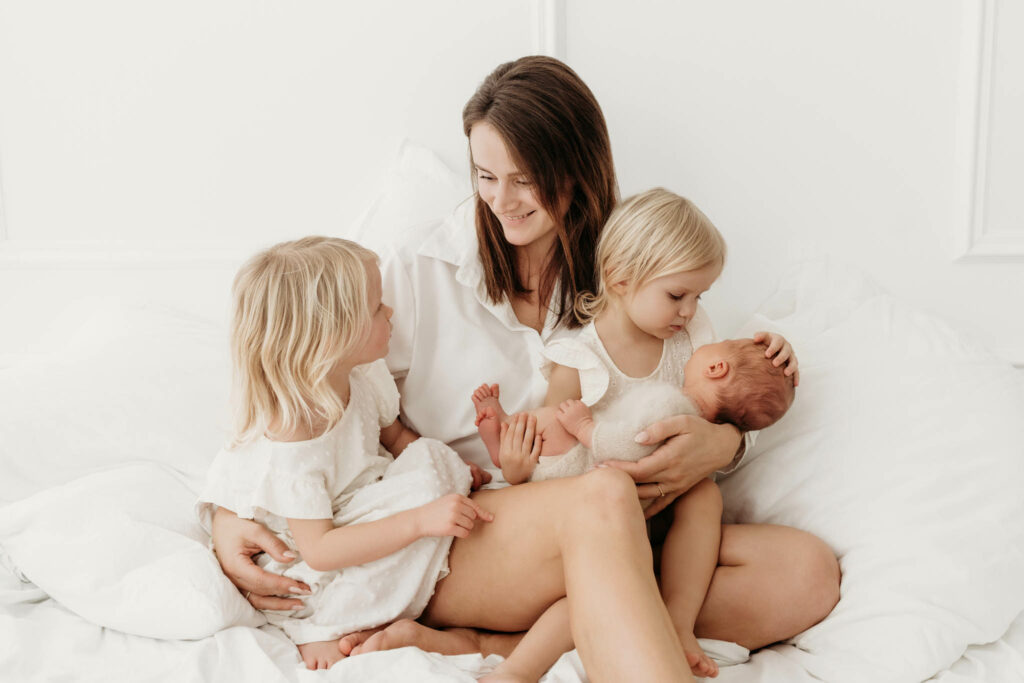 Mama kuschelt mit Geschwisterkindern und Neugeborenen im Bett
