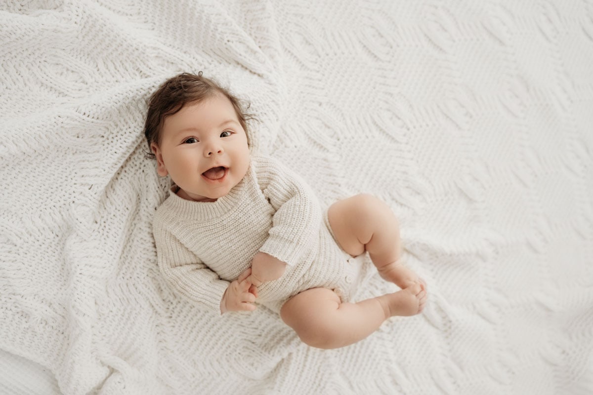 Baby liegt auf Decke, strahlt und lacht