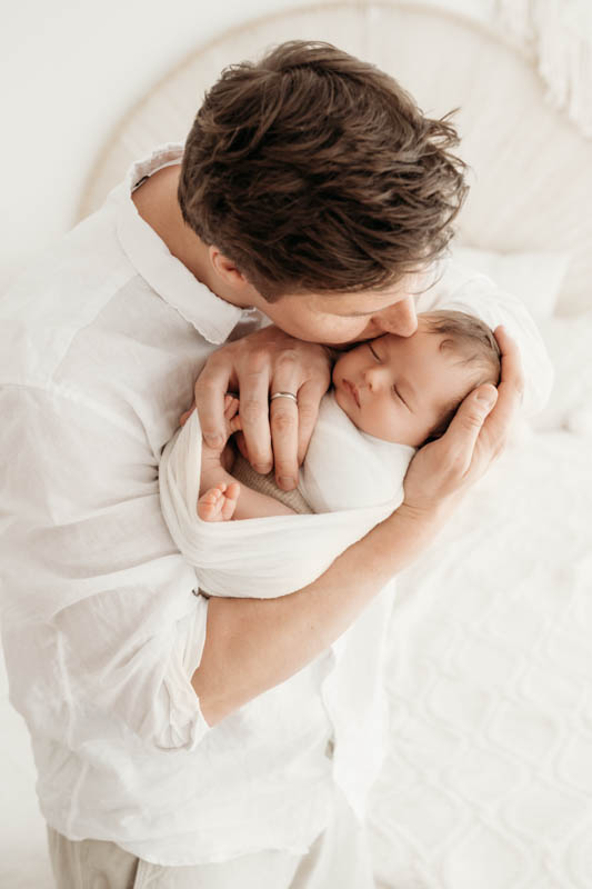 Papa küsst Baby Vater hält sein neugeborenes Baby im Arm und küsst es auf die Stirm