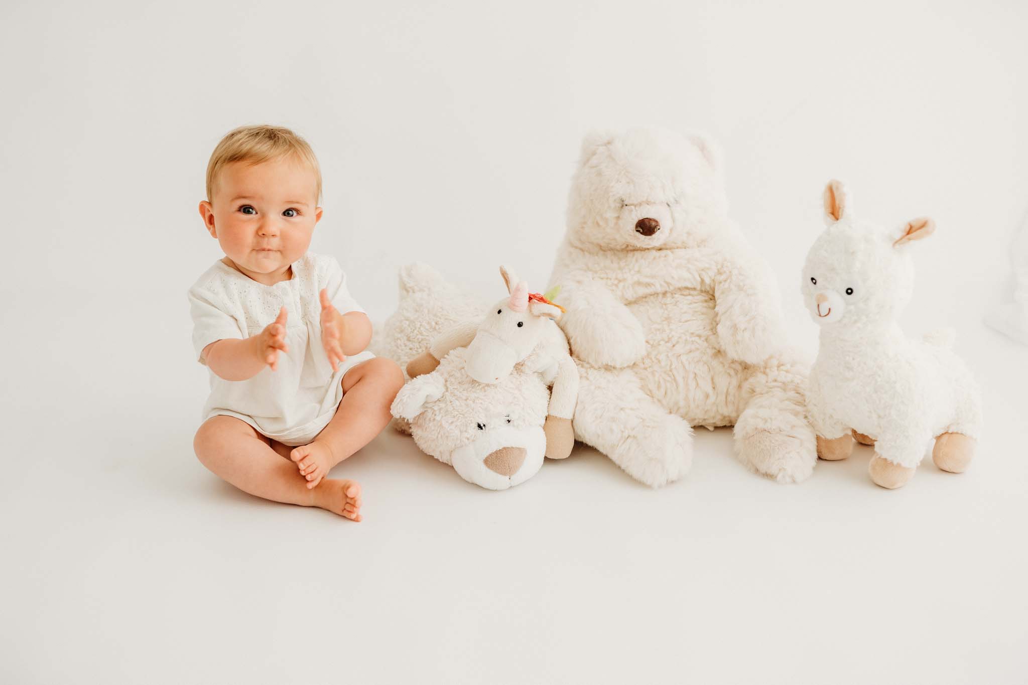 sitzendes Baby klatscht inmitten von Kuscheltieren