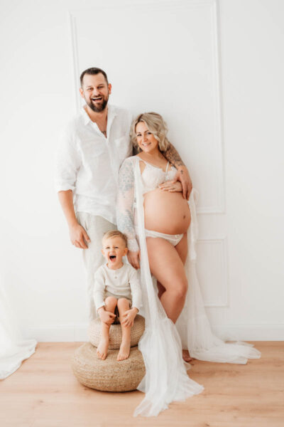 Familie lachend beim Babybauch-Shooting Graz im weißen Studio