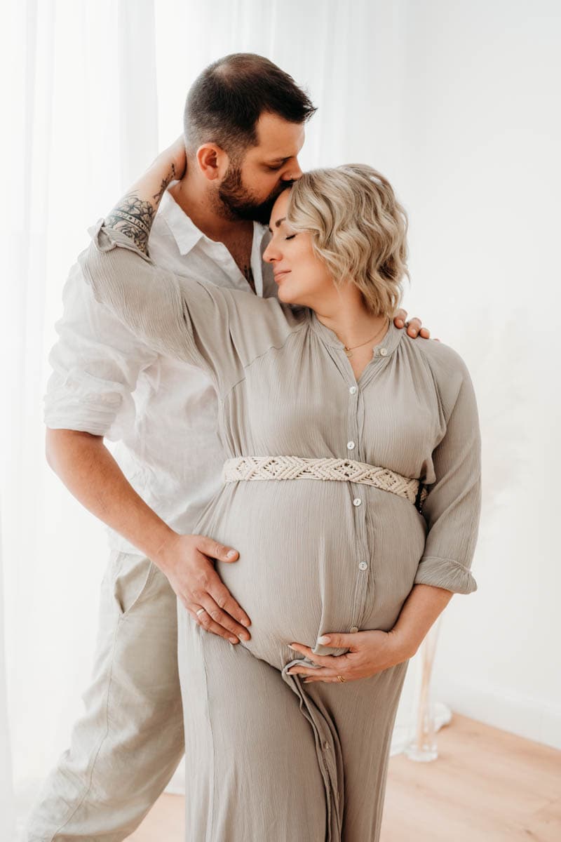 Schwangere Frau schmiegt sich beim Babybauchshooting an Mann und zieht ihn zu sich Schwangere Frau schmiegt sich an Mann beim Babybauchshooting Graz