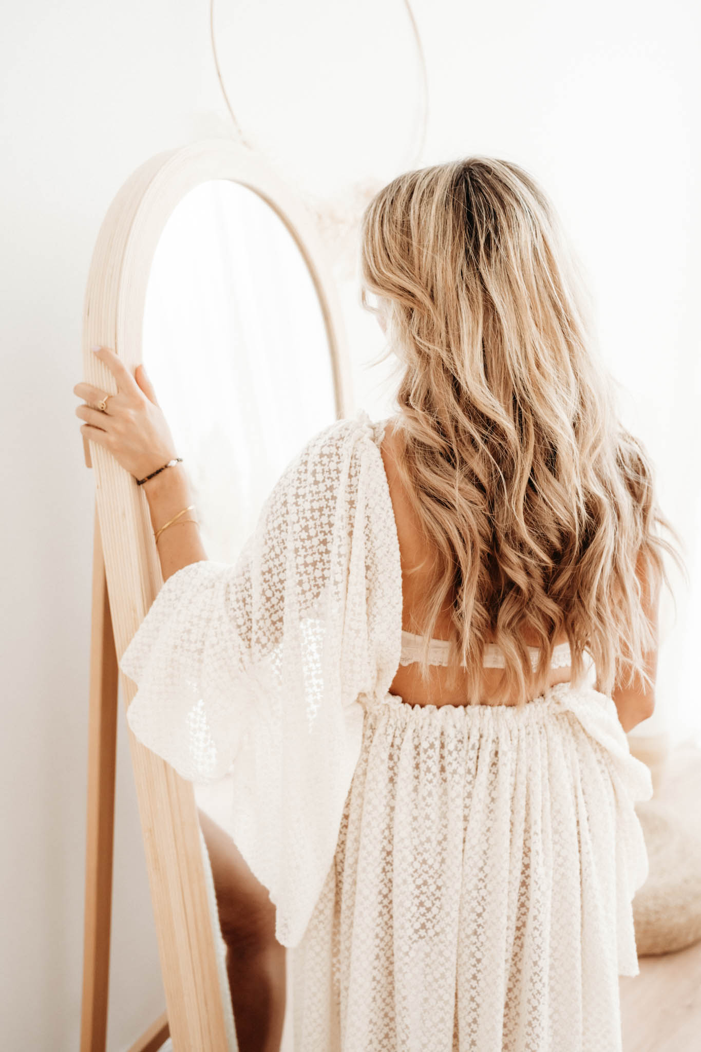 Frau mit blonden Locken vorm Spiegel im Boho Stil bei Babybauchfotografie