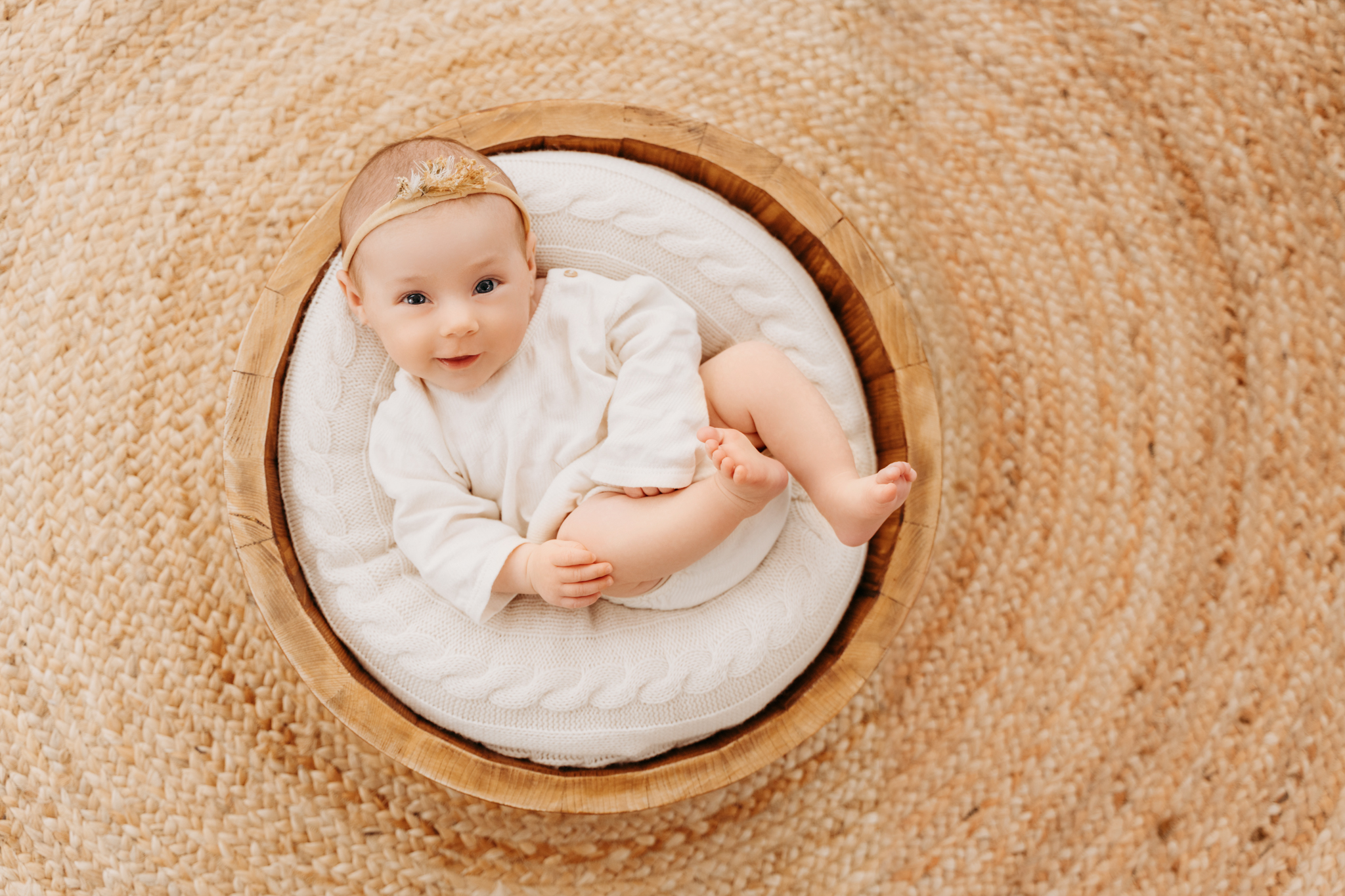 Baby lacht während Babyshooting Graz in die Kamera und liegt in einer runden Holzschale lachendes Baby in runder Holz Schale