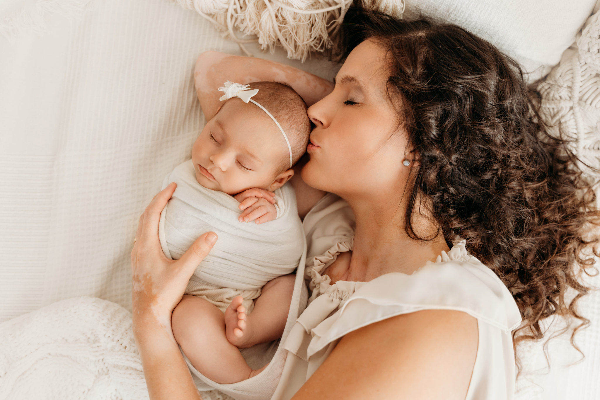 Mama liegt mit Baby beim Newbornshooting im Bett und küsst Babys Kopf Mama küsst kuschelnd neugeborenes Baby auf Stirn