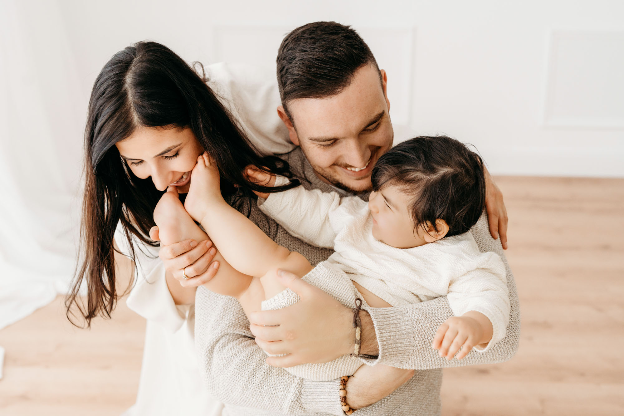 Beim Baby Fotoshooting beißt Mama zärtlich ihr Baby Mama beißt Baby scherzhaft in den Fuß und Papa lacht