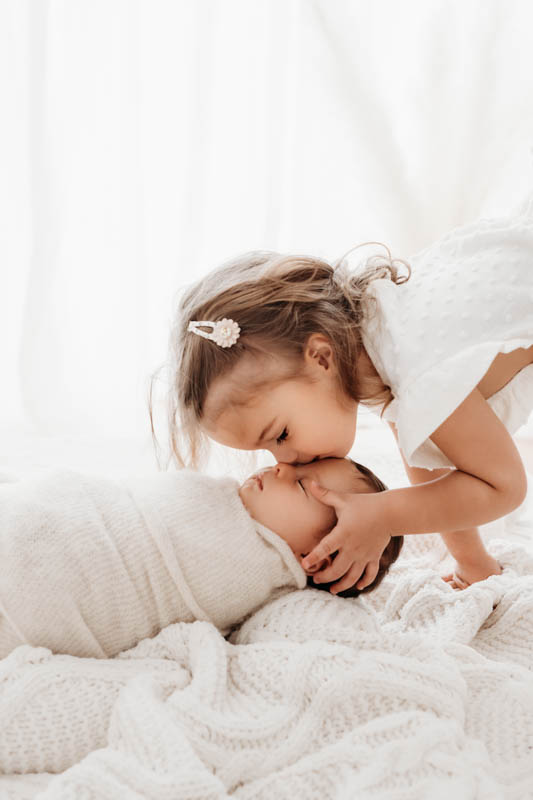 Kleines Mädchen küsst das neugeborene Baby sanft auf die Stirn Kleines Mädchen küsst das neugeborene Baby sanft auf die Stirn
