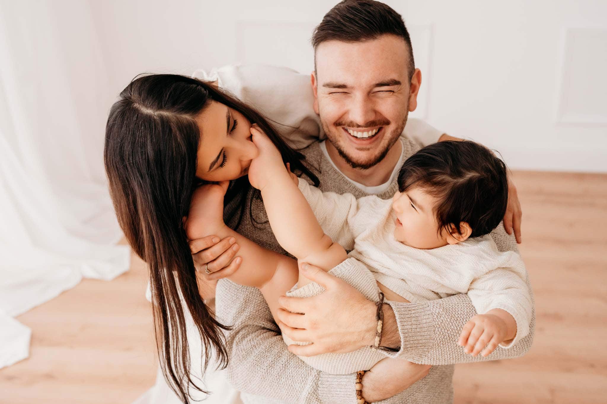 Beim Baby Fotoshooting beißt Mama zärtlich ihr Baby Mama beißt Baby scherzhaft in den Fuß und Papa lacht