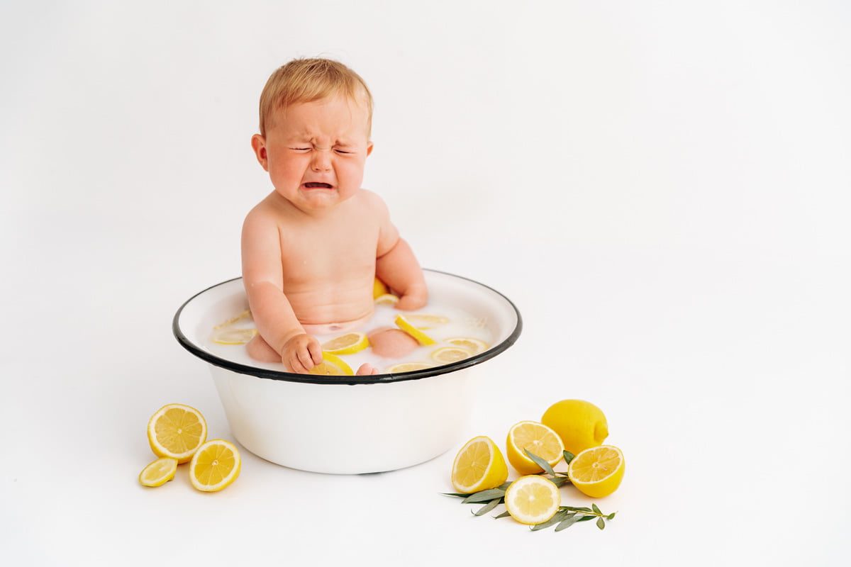 Baby hat in saure Zitrone gebissen beim Milchbad Babyshooting Baby weint im Milchbad voller Zitronen beim Babyshooting