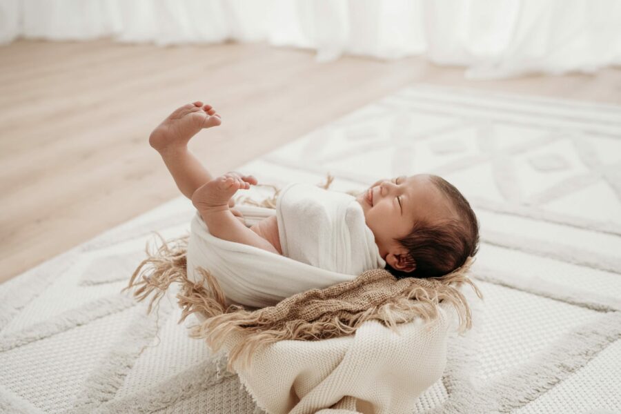 Lachendes und sich streckendes Baby in Holzschale beim Newbornshooting Graz