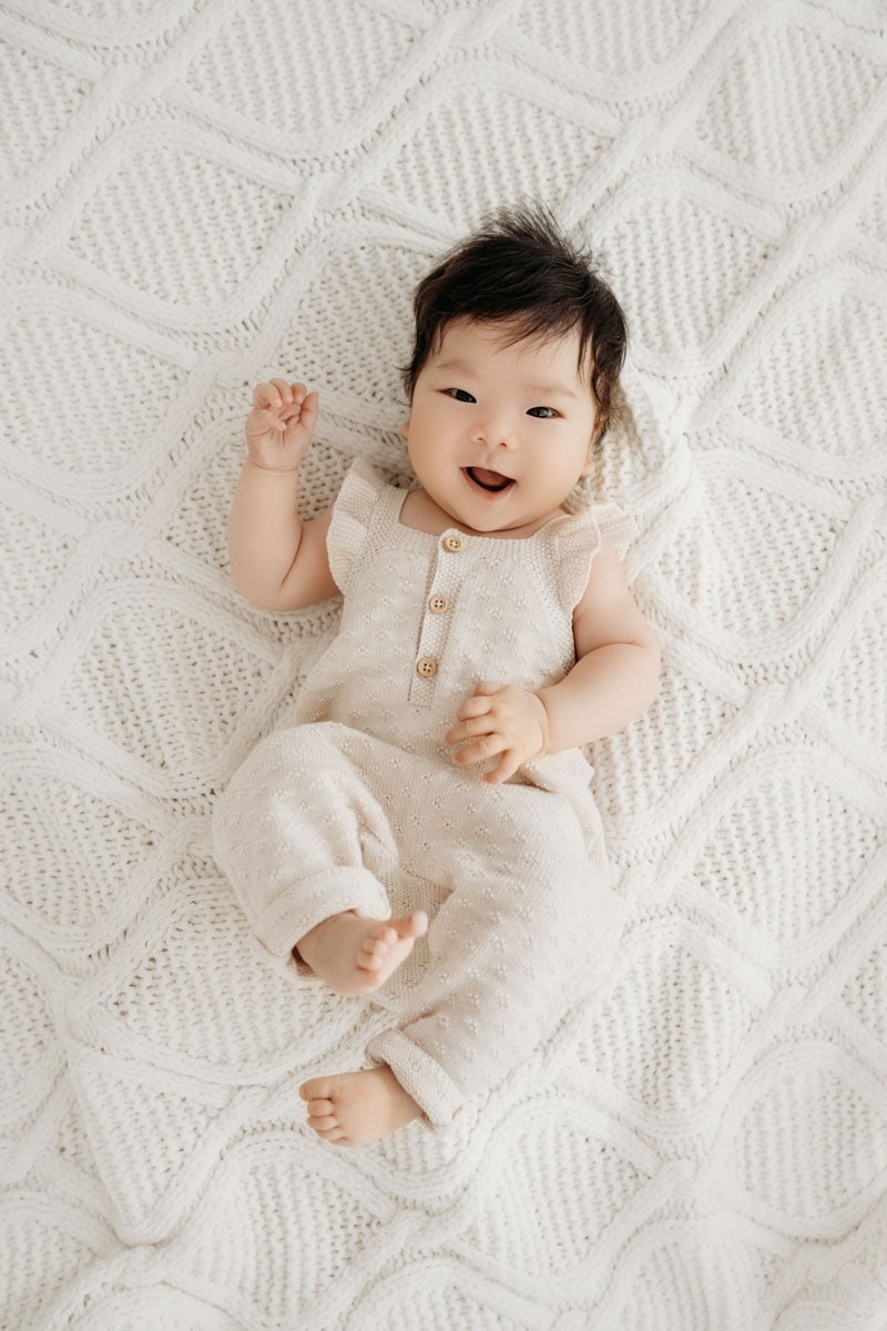 herzlich lachendes Baby auf heller Decke Boho Stil