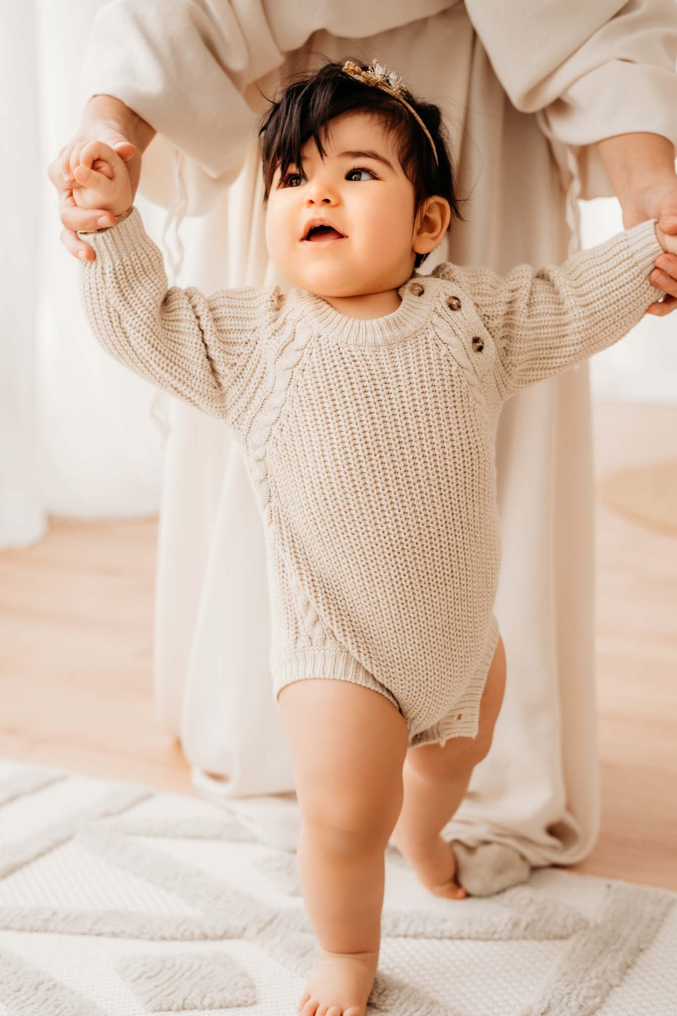 Baby mit vielen schwarzen Haaren macht erste Schritte an Mamas Hand